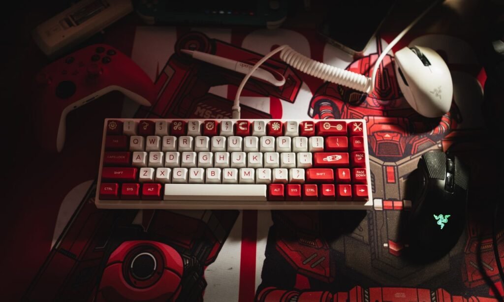 Current image: Close-up of a mechanical keyboard with red and white keys alongside gaming peripherals on a themed desk mat.