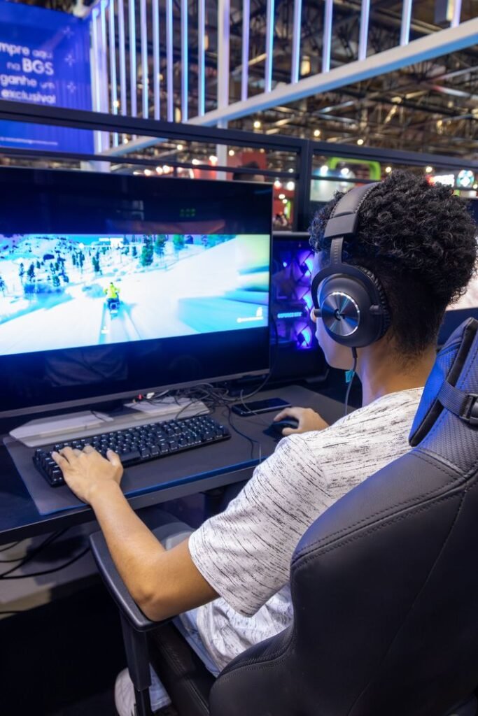 Teen playing video games on a desktop computer with headphones in a lively setting.