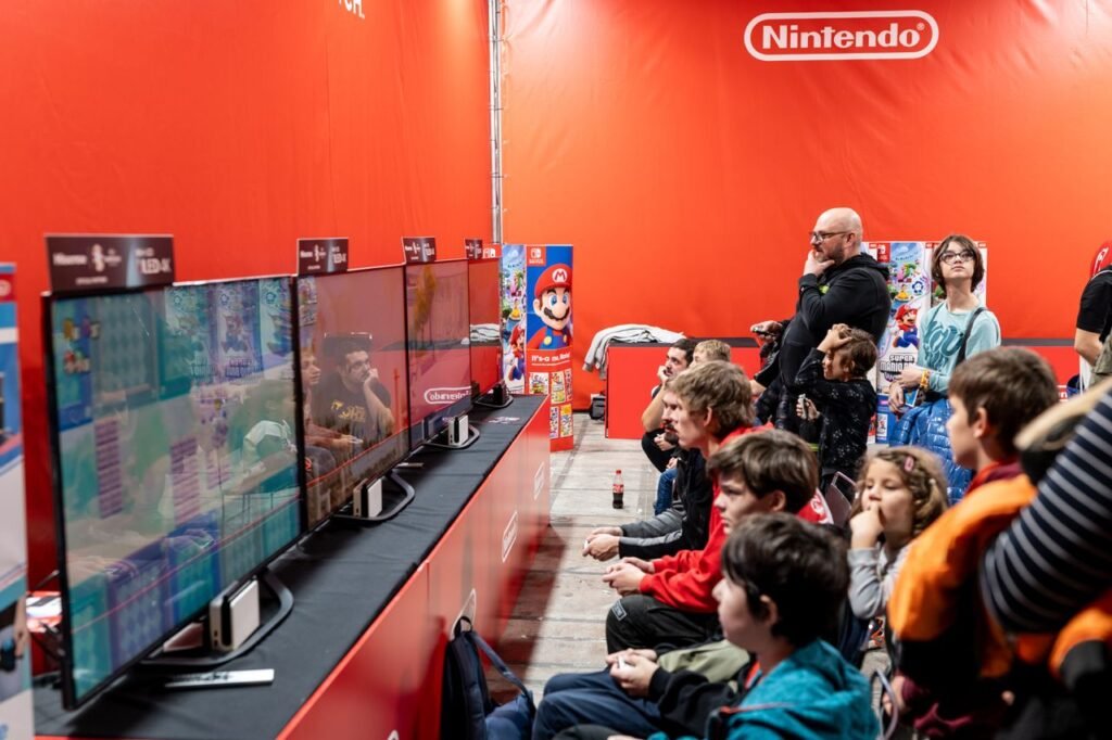 Current image: A lively group enjoys gaming at a Nintendo event in Zagreb, featuring multiple screens and vibrant atmosphere.