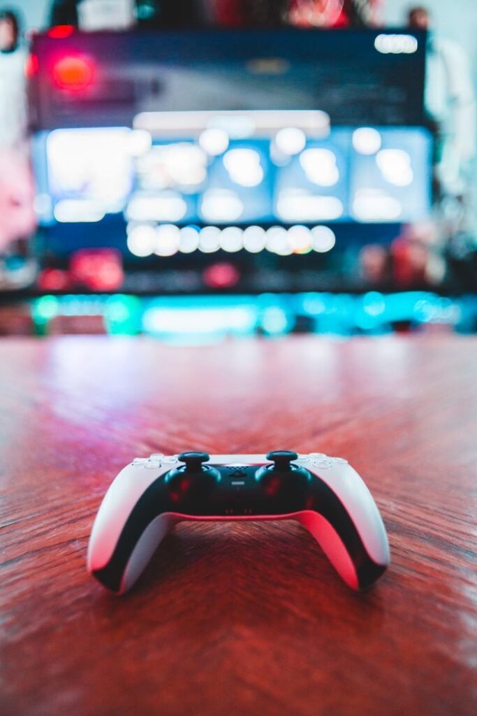 A close-up of a gaming controller on a wooden table with vibrant screen in the background.